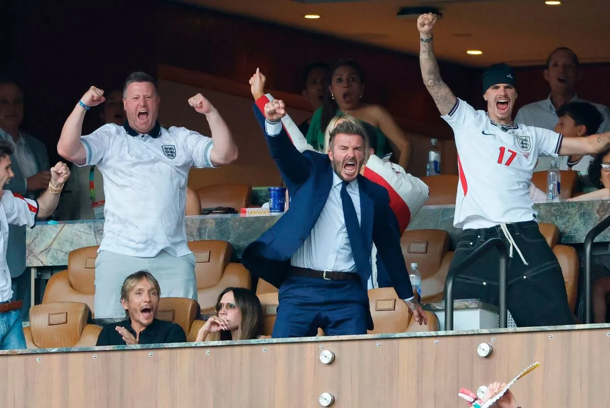 Spectators in a sports stadium, including individuals in formal attire, celebrate enthusiastically with raised arms, likely in response to a significant event or score during a match.